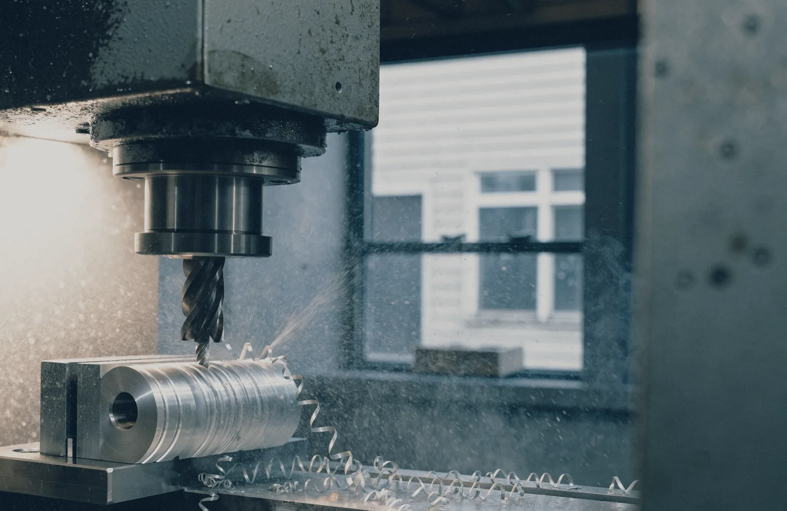 A milling head cutting an aluminium part on a machine bed, swarf curling away from the tool.