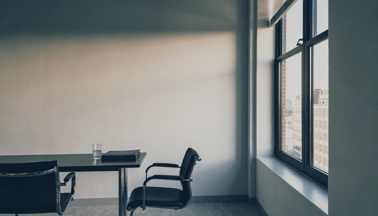 An empty meeting room with two chairs at a small table beside a tall window.